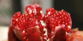Ile kalorii ma granat? Zbliżenie rozłupanego granatu, odsłaniające skupiska jasnoczerwonych, soczystych nasion wewnątrz ciemnoczerwonej skórki - idealne do podkreślenia granatu wartości odżywczych.